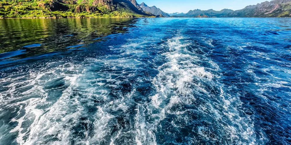 The hybrid-electric boat's wake trailing across the silent fjord
