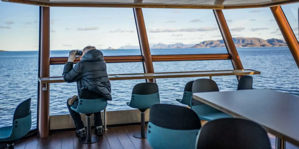 Guests in the warm panoramic indoor lounge watching the fjord glide by