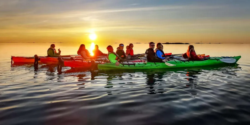 A line of kayaks pausing to watch the midnight sun touch the horizon