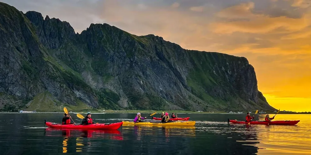 Kayakers on the open ocean below Lofoten mountains in golden light