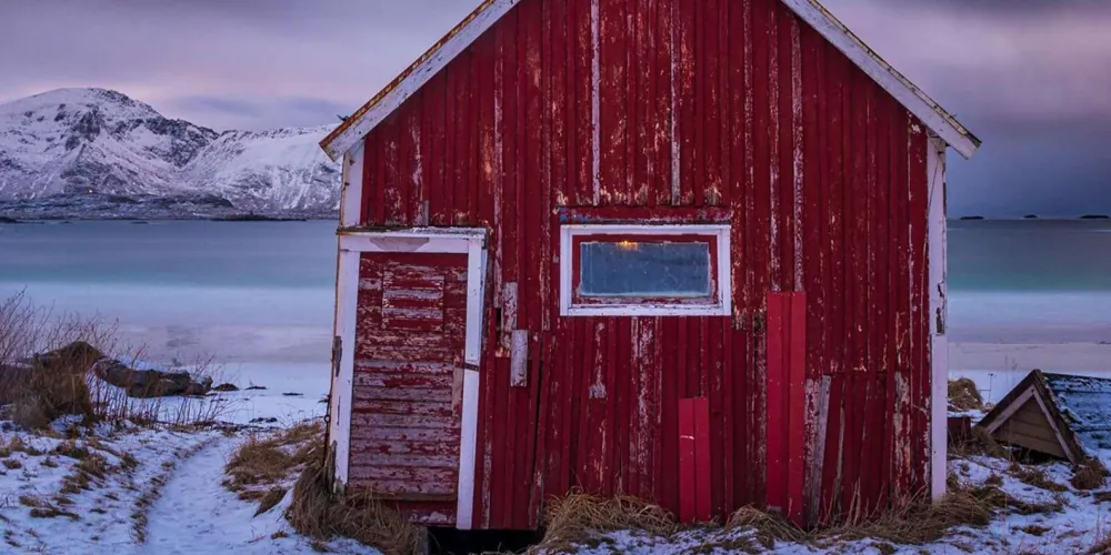 A lone red boathouse on the rocky Lofoten shoreline